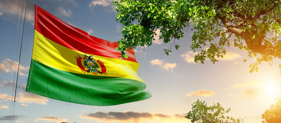 Bolivia national flag waving in the sky behind the tree. The flag blow in beautiful sunlight. Bolivia national flag for independence day.