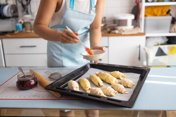 Female baker smears raw croissants with a brush in the yolk, the cooking process.