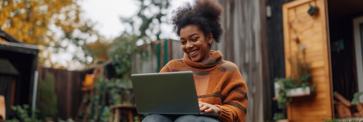 Wall Mural - A woman is sitting on the ground with a laptop in front of her. She is smiling and she is enjoying herself