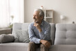© fizkes - Dreamy pensive elderly gray-haired man relaxing alone at home, sitting on couch, looking into distance with candid smile, having nostalgic mood, reminiscing, feel satisfied on carefree retired life
