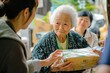 © siripimon2525 - A Japanese elder receiving a donation package from a community volunteer, with one hand gently grasping the package and the other resting on the volunteer hand in gratitude, surrounded by other