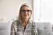 © fizkes - Head shot portrait attractive mature woman in glasses sit on sofa looking at camera, take part in telemedicine appointment with doctor, get consultation, engaged in communication with family, webcam