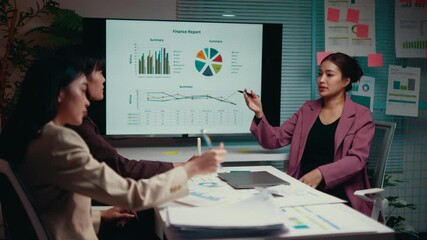 Wall Mural - Businesswomen team working late reviewing financial report, using digital devices and pointing at graphs displayed on a screen in a meeting room