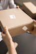 © fizkes - Close up view unknown female hands giving, receiving cardboard package. Client takes box in postal services. Workflow of post office or warehouse worker. Parcel shipping management, orders fulfilment