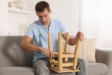 Canvas Print - Man repairing wooden stool with screwdriver indoors