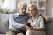 © fizkes - Serious focused aged couple sit on sofa with smartphone, learn software, new mobile application or platform, review e-bank account statement. Retired family people and modern wireless technology usage