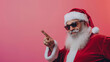 © Michael - Santa claus in sunglasses points to the left against a pink backdrop