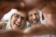 © fizkes - Close up faces happy older couple make heart symbol with fingers, feeling unconditional love, express support in relationships. Advertise dental clinic and heart check-up professional medical services