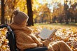 © Exclusive  - Sitting in a wheelchair, an elderly woman reads a book while wrapped in a cozy sweater in a park filled with colorful autumn leaves under the sun