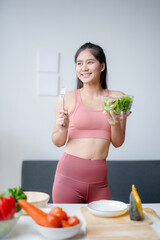 Wall Mural - Young woman in activewear is holding a salad bowl and fork, smiling while thinking about her healthy meal