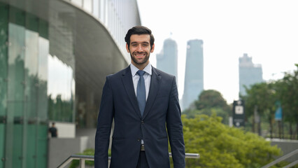 Wall Mural - Professional businessman standing at city or park. Smiling project manager looking at camera while smiling arms with confident. Closeup of investor wearing suit at architectural building. Exultant.