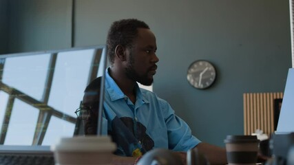 Young African American programmer wearing casual shirt working on computer in modern IT company office