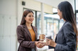© bunyiam - Two women shaking hands and holding coffee cups