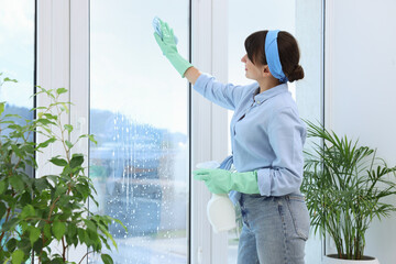 Canvas Print - Beautiful young woman with spray bottle of detergent and napkin cleaning window indoors