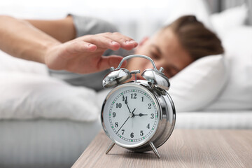 Man turning off alarm clock in bedroom at lunch time, selective focus