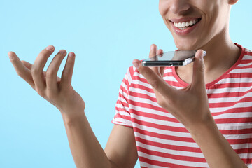 Poster - Young man recording voice message via smartphone on light blue background, closeup