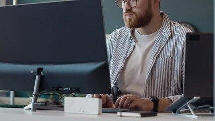 Medium shot of young Caucasian sysadmin with beard on face typing on desktop computer in IT company office