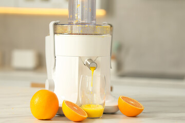 Modern juicer, oranges and glass on white marble table in kitchen