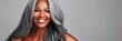 © Elmira - A beautiful mature black woman with glowing skin and long silver-gray hair smiles warmly, radiating confidence and elegance in a simple, neutral setting