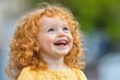 © Konstiantyn Zap - Joyful Redheaded Toddler Laughing Outdoors in Natural Light, Curly Hair, Happiness, Childhood, Green Background