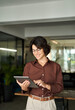 © insta_photos - Smiling busy young adult Hispanic businesswoman, female professional executive leader or entrepreneur, happy lady company worker using tablet working standing in modern office. Vertical photo.