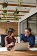 © insta_photos - Two busy business team people using laptop computer working together sitting at office meeting. Happy young woman and mature man entrepreneurs executives smiling at work talking in workspace. Vertical