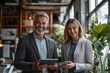 © yj - two happy busy business man and woman executives partners team working together standing in office using digital tablet in corporate cooperation on company project.