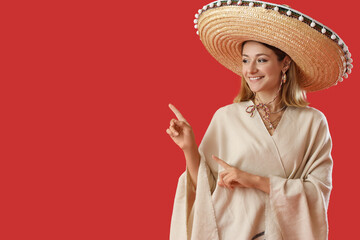 Sticker - Pretty young woman in sombrero and poncho pointing at something on red background