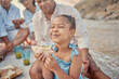 © Lumeez23/peopleimages.com - Picnic, child and smile on beach with sandwich, happiness and excited with family. Kid, wellness and food in nature for nutrition, favorite snack and lunch on outing for travel and fun in Brazil