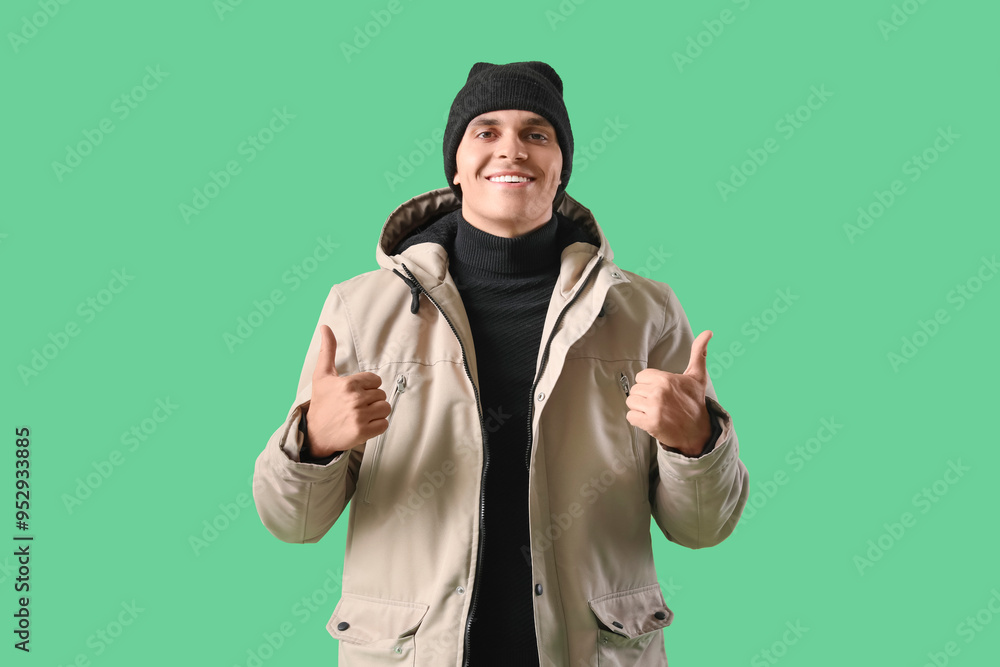 Young man in winter clothes showing thumbs-up on green background