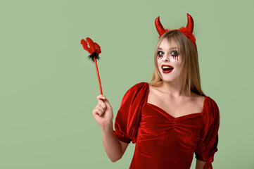 Wall Mural - Young woman dressed for Halloween as devil with trident on green background