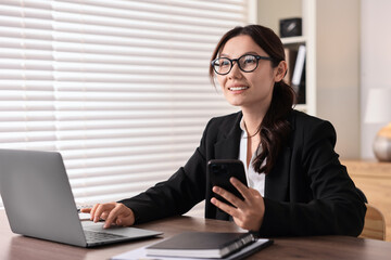 Smiling businesswoman with smartphone at table in office