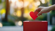 © Nemanja - Woman hand holding a heart above donation box, symbolizing charity, care, and community support, with copy space for text, concept of giving, help, and hope