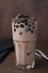 Wall Mural - Tasty milk bubble tea in glass on wooden table against brown background