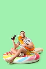 Poster - Young man with binoculars and ring buoy sitting on inflatable mattress in shape of candy against green background