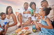 © Lumeez23/peopleimages.com - Happy family, beach and toast with drink at picnic for holiday, summer and lunch. Juice, cheers or people by coast with food for generations, parents or kids with grandparents at celebration to relax