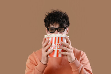 Wall Mural - Young man in 3d eyeglasses with popcorn on brown background