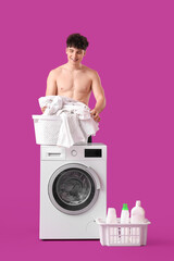 Wall Mural - Young man in underpants with laundry basket near washing machine on pink background