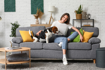 Poster - Young woman with cute Beagle dog sitting on sofa in living room