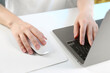 © New Africa - Woman using computer mouse while working with laptop at white table, closeup