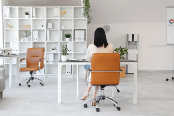 Wall Mural - Young woman using modern laptop and sitting at workplace in light office