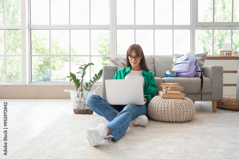 Happy female student with backpack, books and laptop studying at home