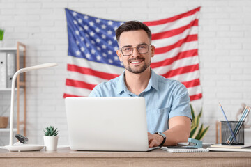 Sticker - Handsome young happy man with laptop and flag of USA working at table in office