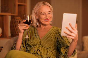 Canvas Print - Mature woman with wine and tablet computer having online date at home in evening