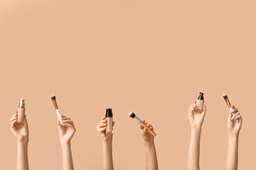 Wall Mural - Female hands with bottles of makeup foundation and brushes on brown background