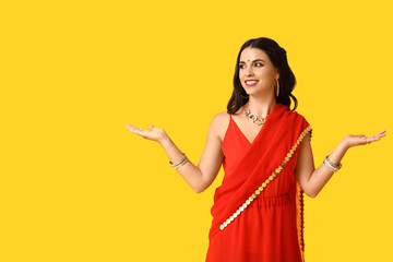 Wall Mural - Beautiful young happy Indian woman in traditional sari dancing on yellow background. Divaly celebration