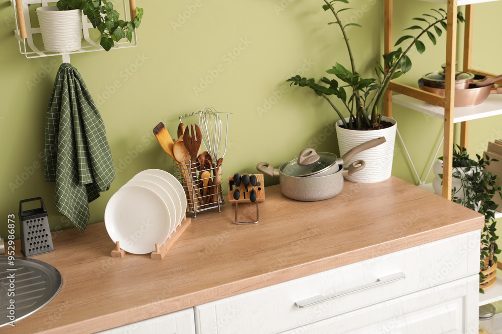Utensils with plant on counter near green wall in kitchen