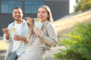 Poster - Young colleagues eating Asian noodles during lunch break outdoors