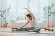 © Monster Ztudio - Happy young Asian woman practicing yoga and shoulder stretching at home sitting on floor in living room