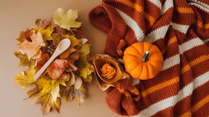 Wall Mural - A photo of a flat lay with a beige background. There is a pumpkin knit blanket in the center. The overall image has a warm, autumnal color palette.